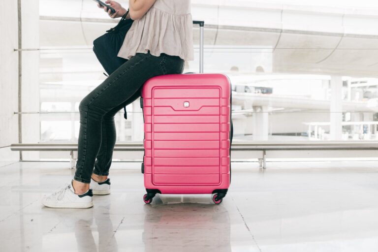 woman in white top and denim jeans sitting on red luggage bag